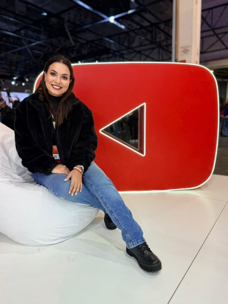 Camila Mecenas sentada ao lado do logo do YouTube em evento do mercado digital
